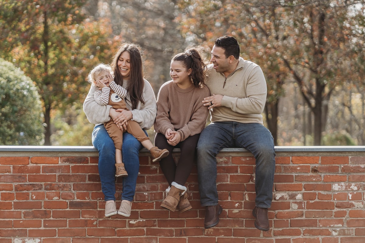 silly family photo mother, son, daughter, father sitting on a brick wall ledge.