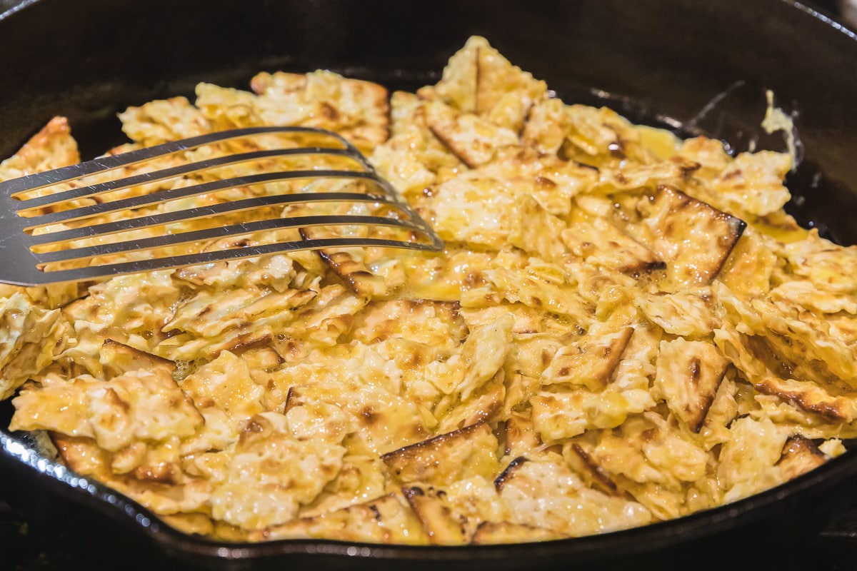 uncooked matzo brei in a cast iron skillet with a metal spatula.
