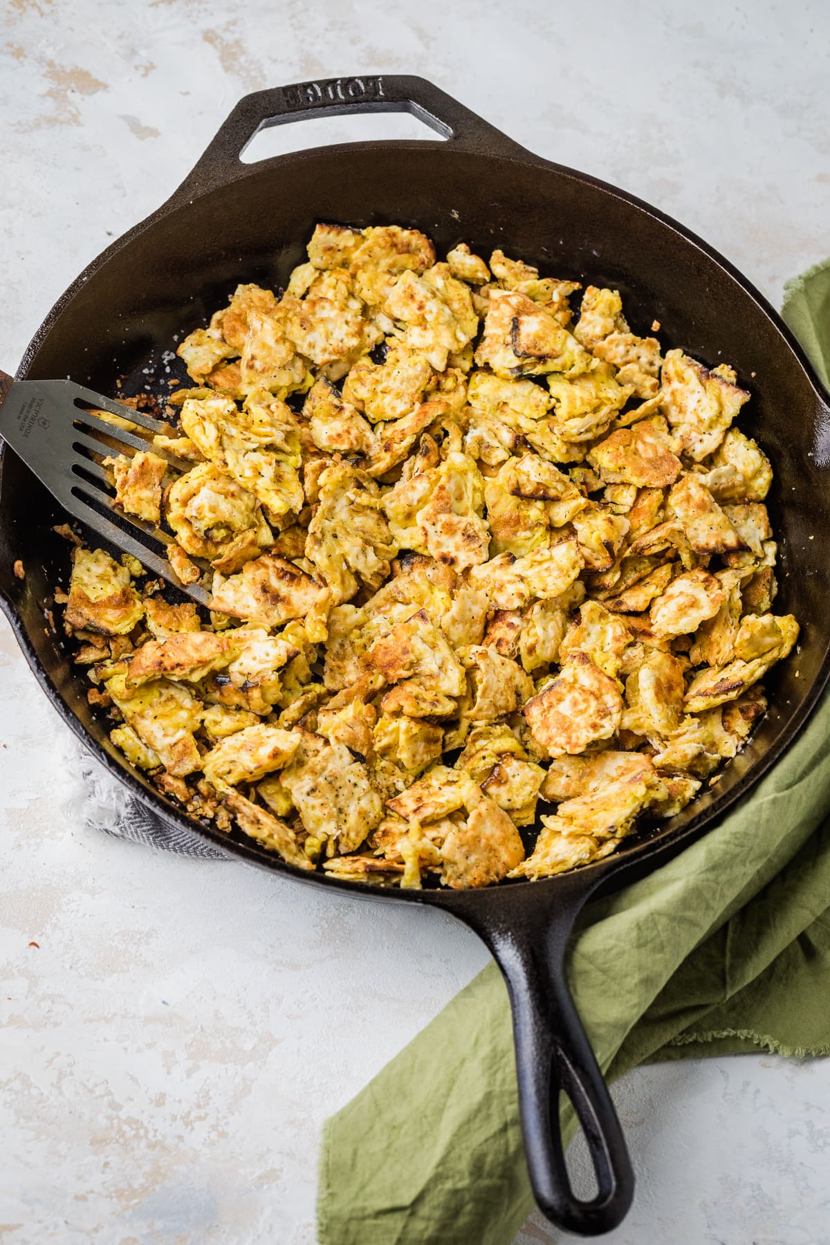 matzo brei in a cast iron skillet with a green napkin to the bottom right.