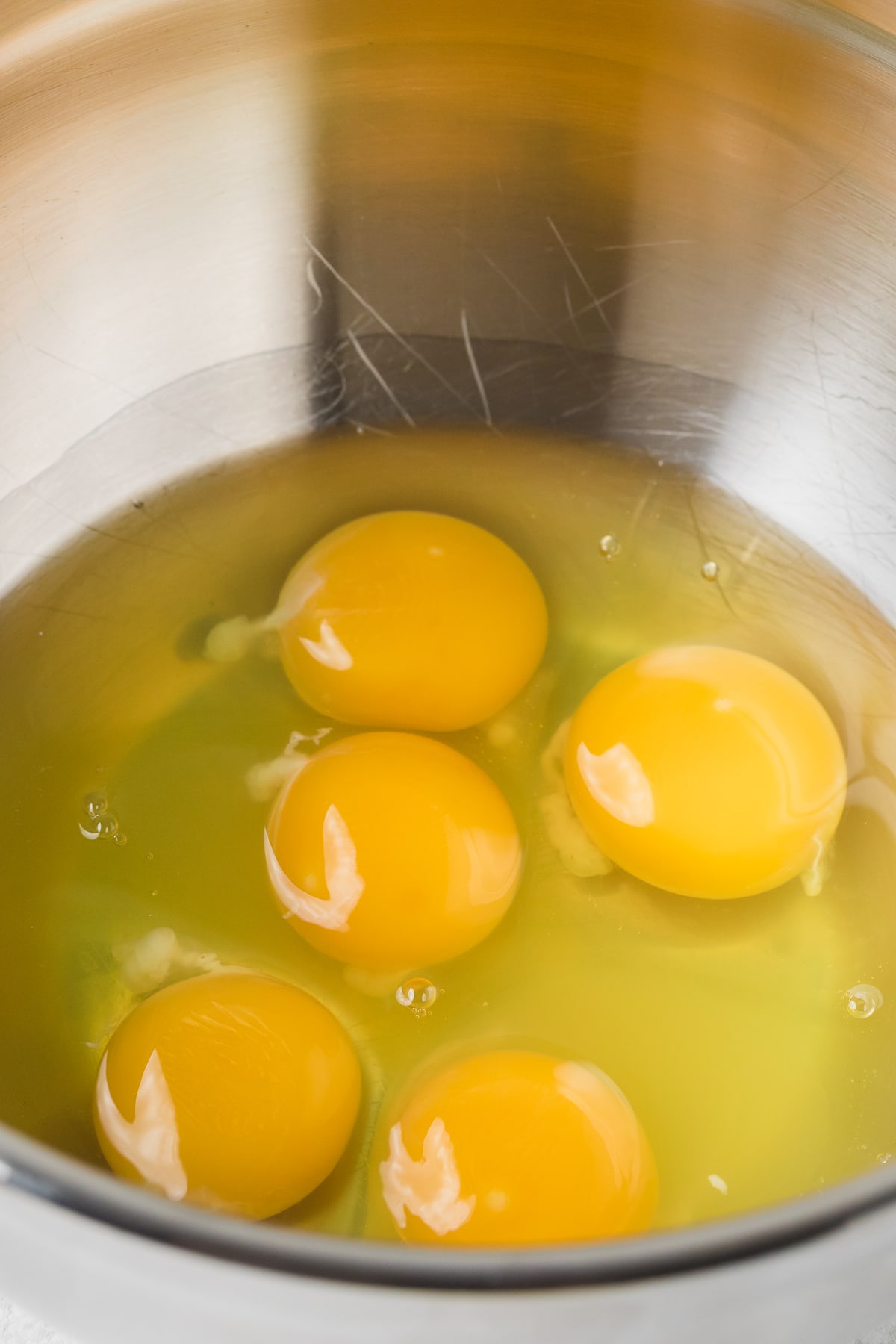 5 raw eggs in a stainless steel mixing bowl.