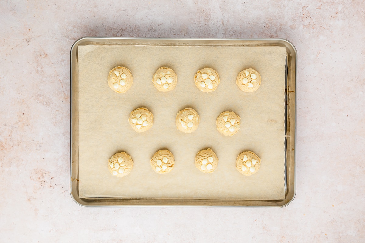 white chocolate chip cookie dough on a parchment lined baking sheet with chocolate chips added to the top to make them look pretty after baking.