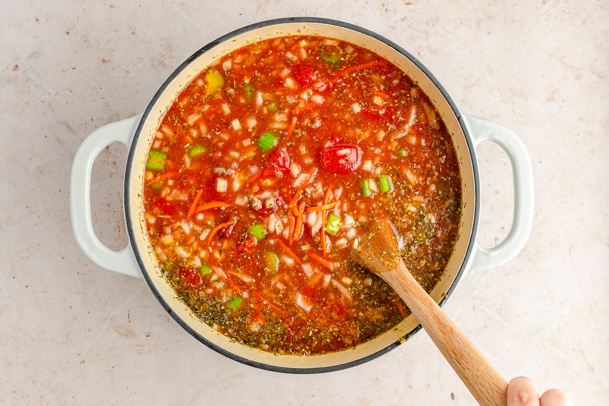 soup cooking in a dutch oven with a wooden spoon inside mixing.