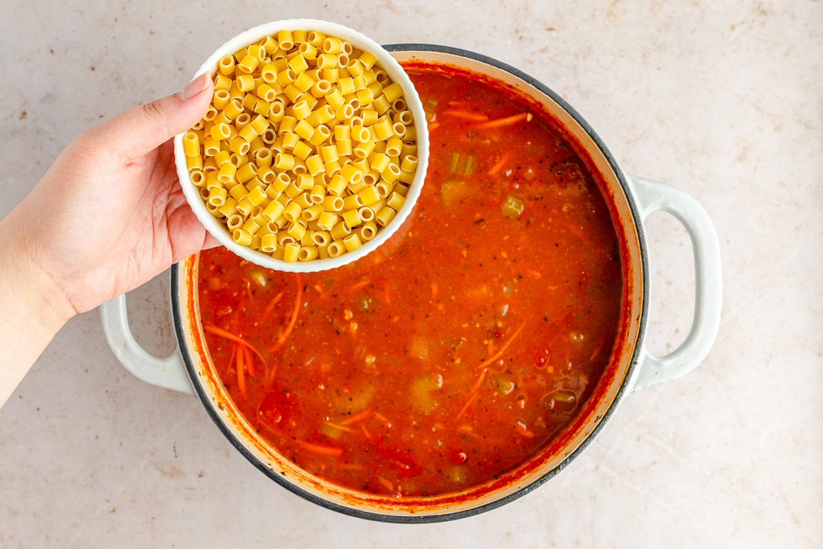 hand holding a bowl of dry pasta to add to soup.