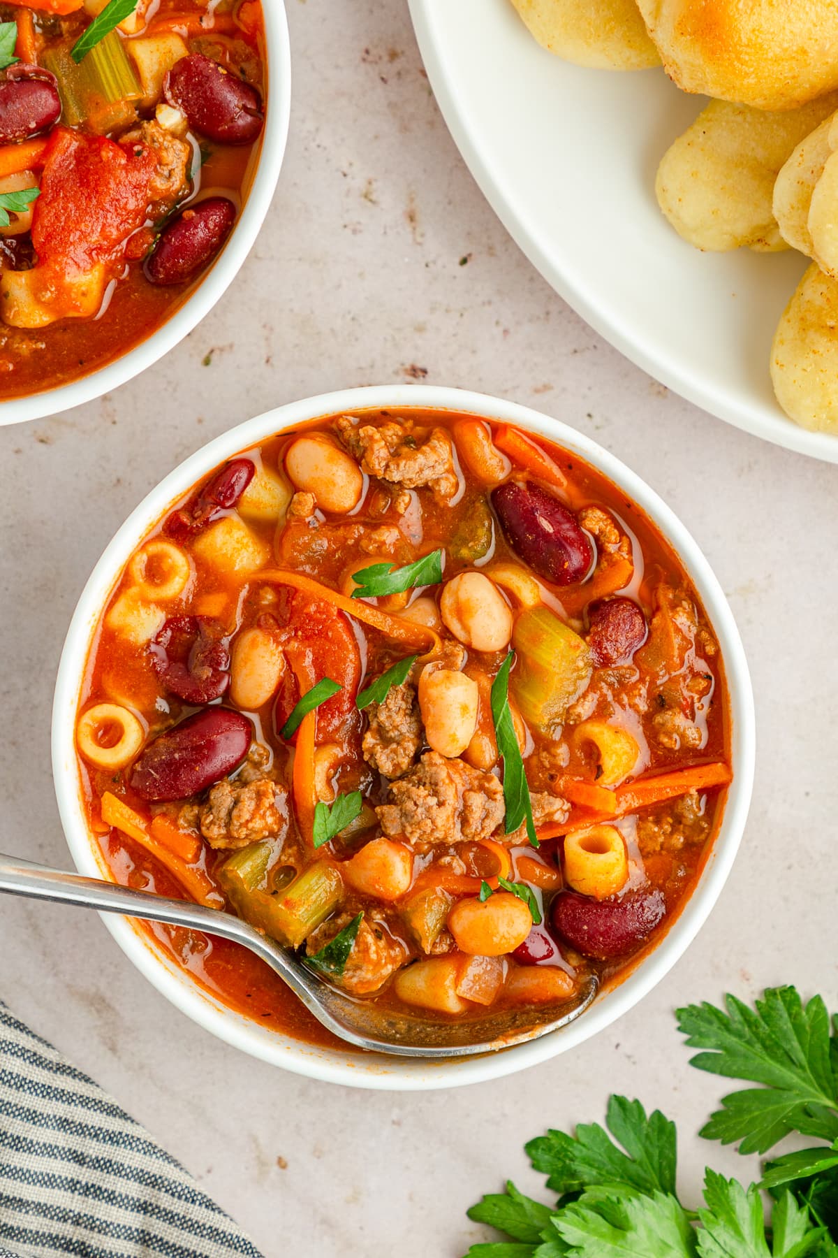 Pasta e Fagioli Soup in a white bowl with a spoon and breadsticks on the side.