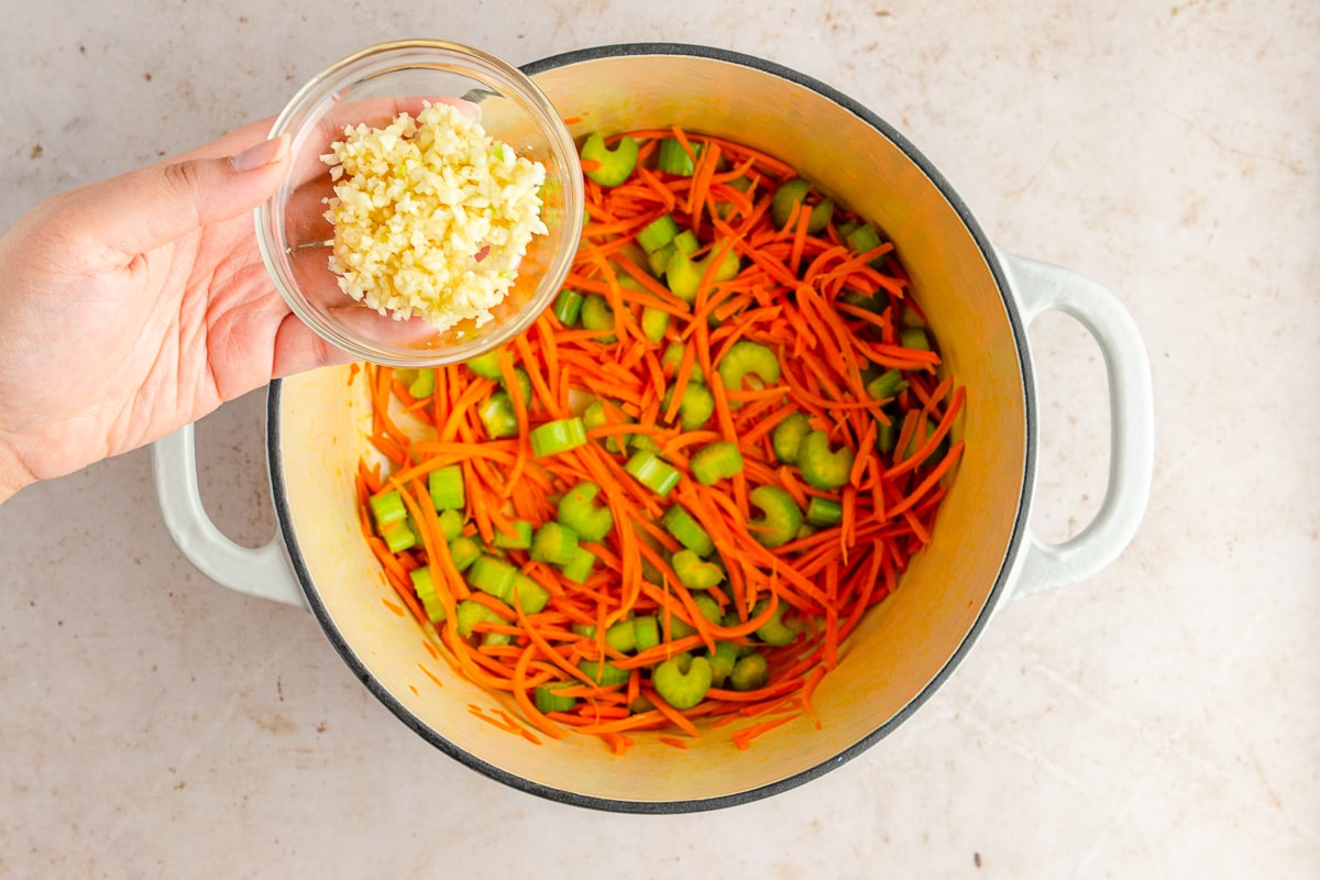 hand holding garlic above cooked veggies in a pot.