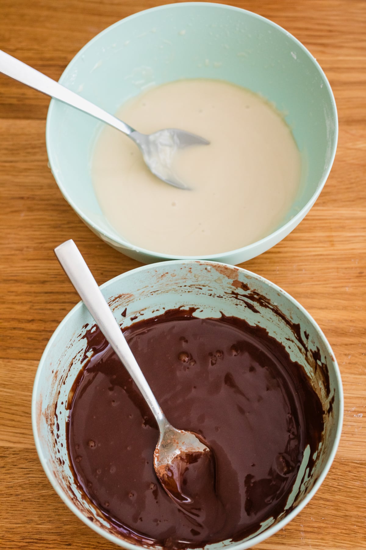 vanilla and chocolate glaze for donuts in light green bowls with spoons on a wooden countertop.