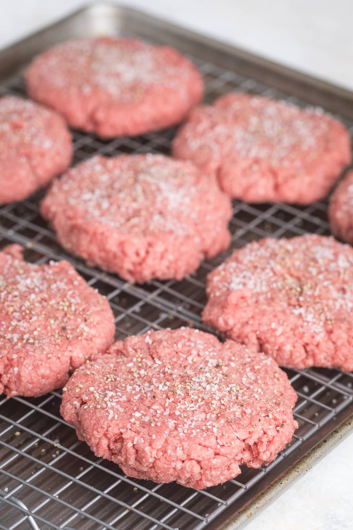 raw hamburger patties on a wire rack ready to be baked with salt and pepper seasoning.