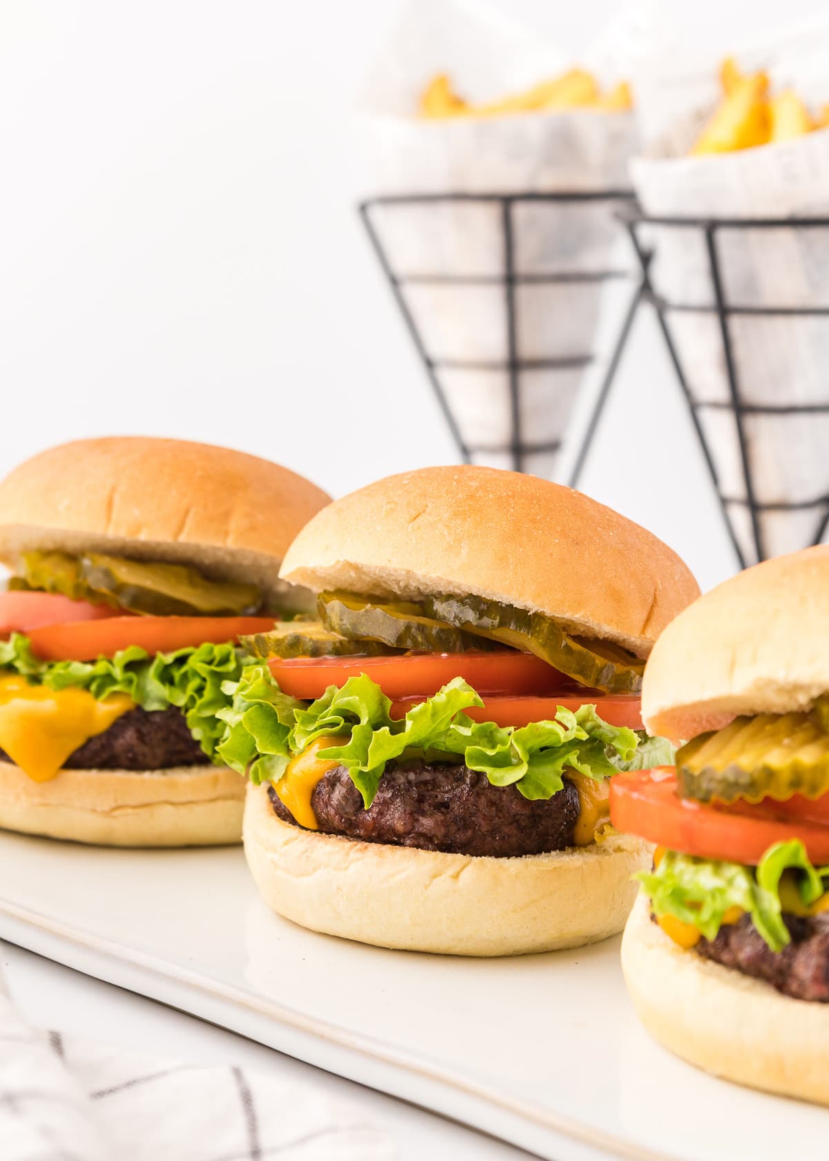 three topped hamburgers with cheese and toppings and fries in the background.