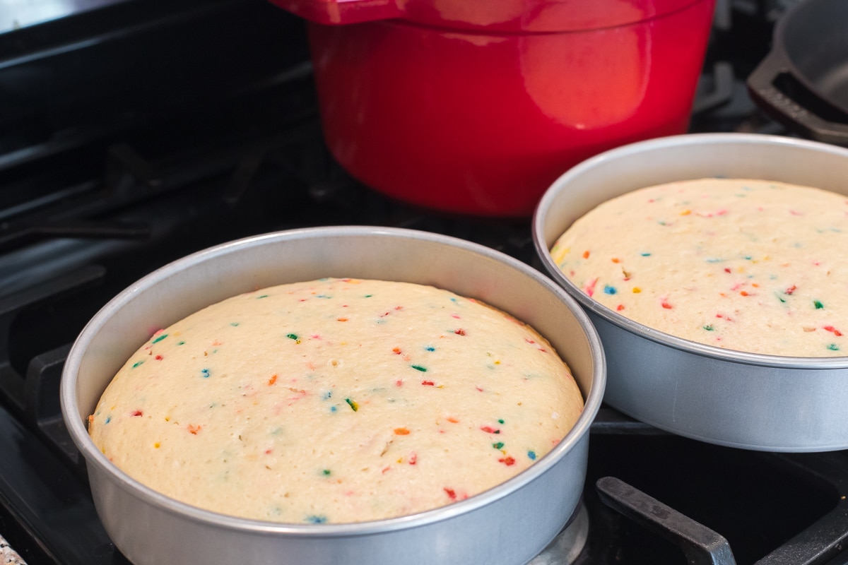 two cake pans with baked cakes cooling on a stovetop.
