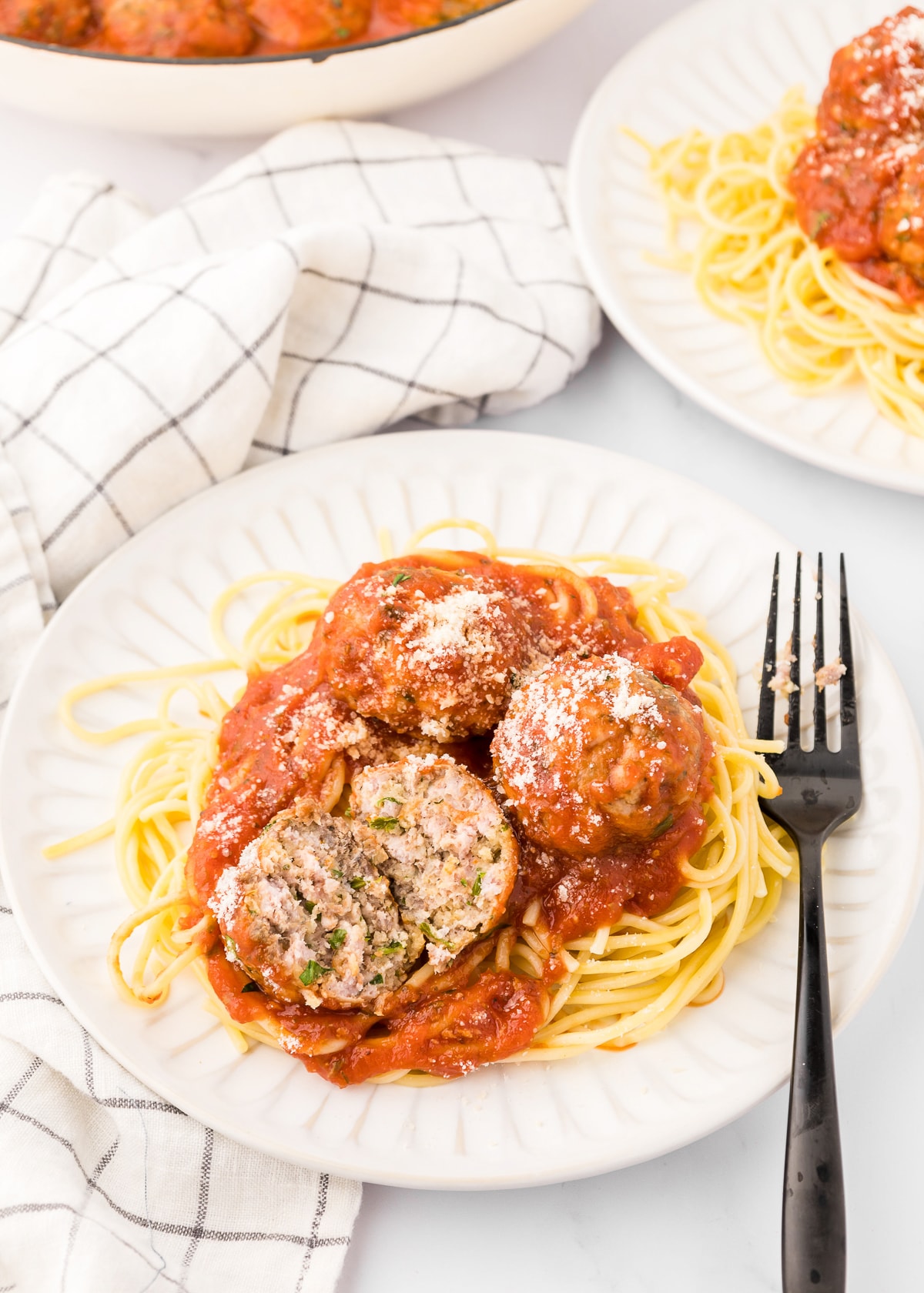 Plate of baked meatballs with one cut in half over pasta with sauce with a black fork on the plate.
