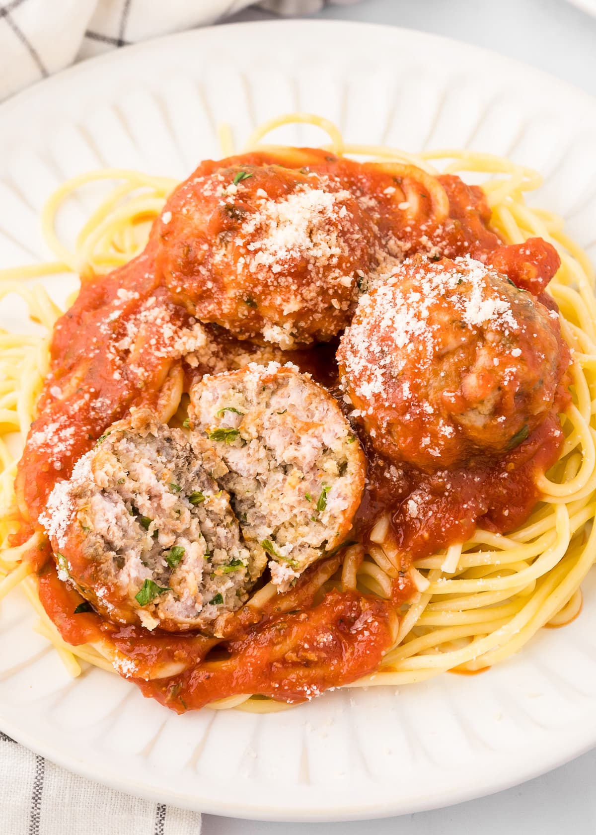 Plate of baked meatballs with one cut in half over pasta with sauce.