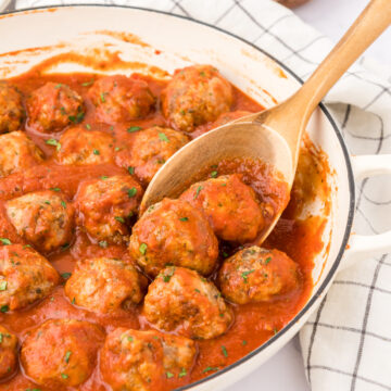 pan of sauced meatballs with wooden spoon holding one.