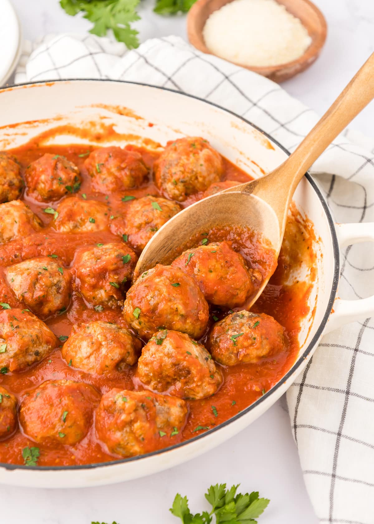 pan of sauced meatballs with wooden spoon holding one.