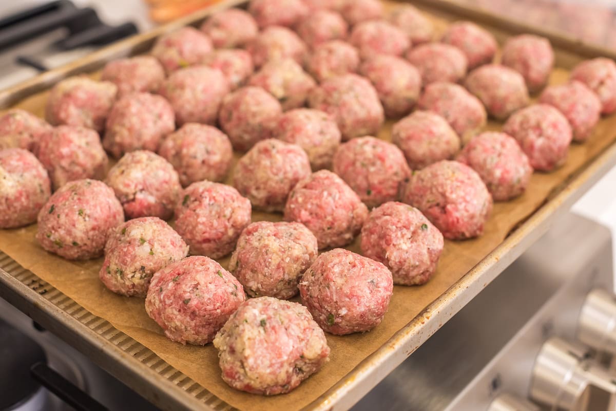 raw italian meatballs on a parchment lined baking sheet on a stovetop.
