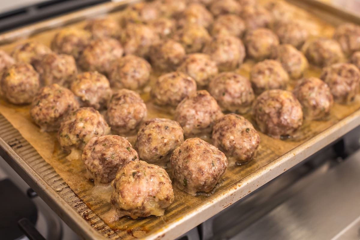 baked italian meatballs on a parchment lined baking sheet on a stovetop.