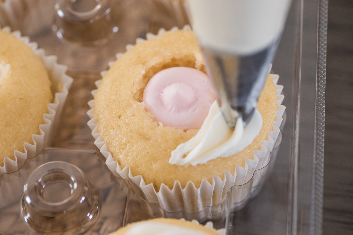 piping frosting over cupcakes filled with pink frosting.