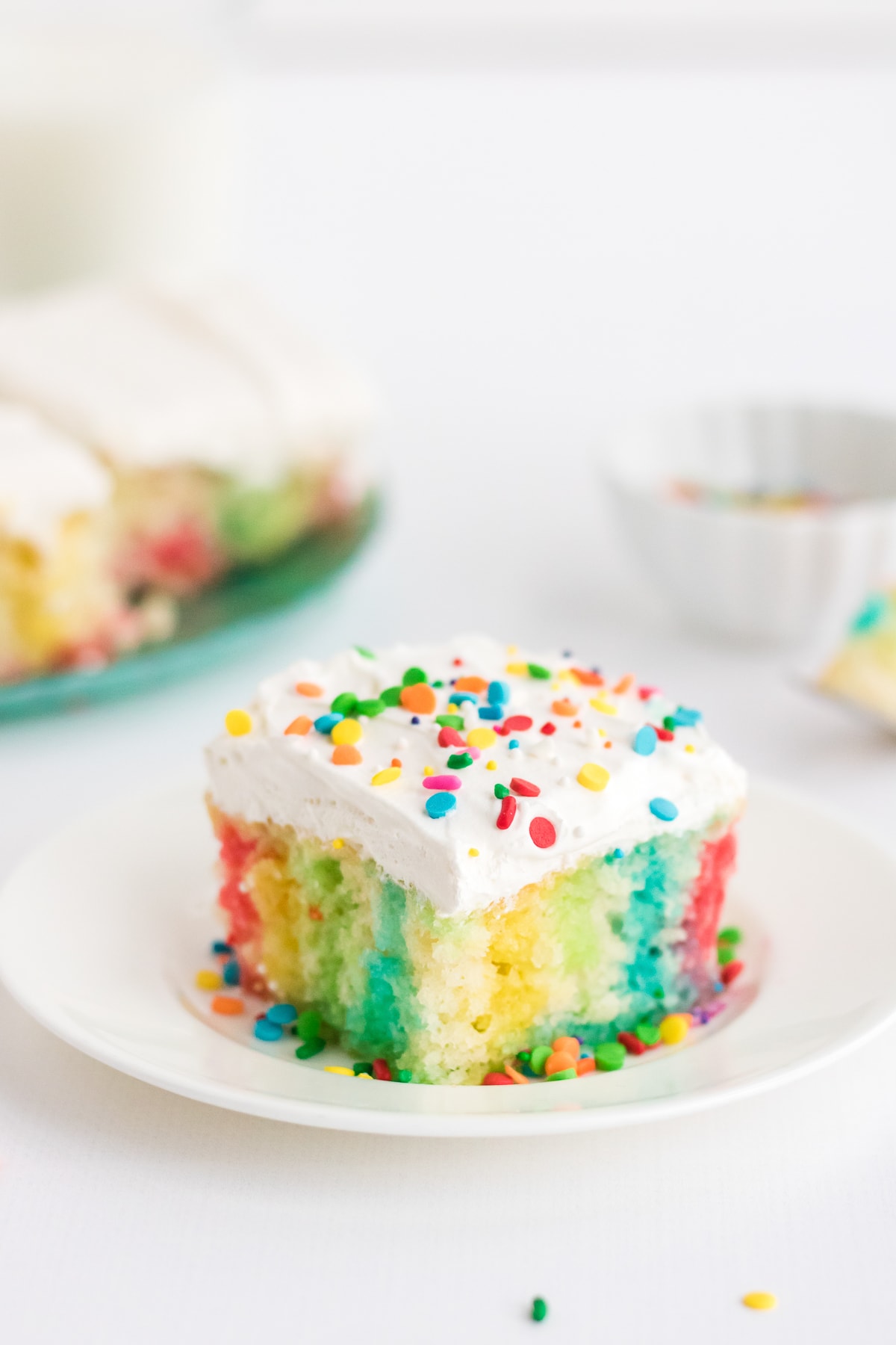 rainbow jello poke cake with whipped topping and sprinkles.