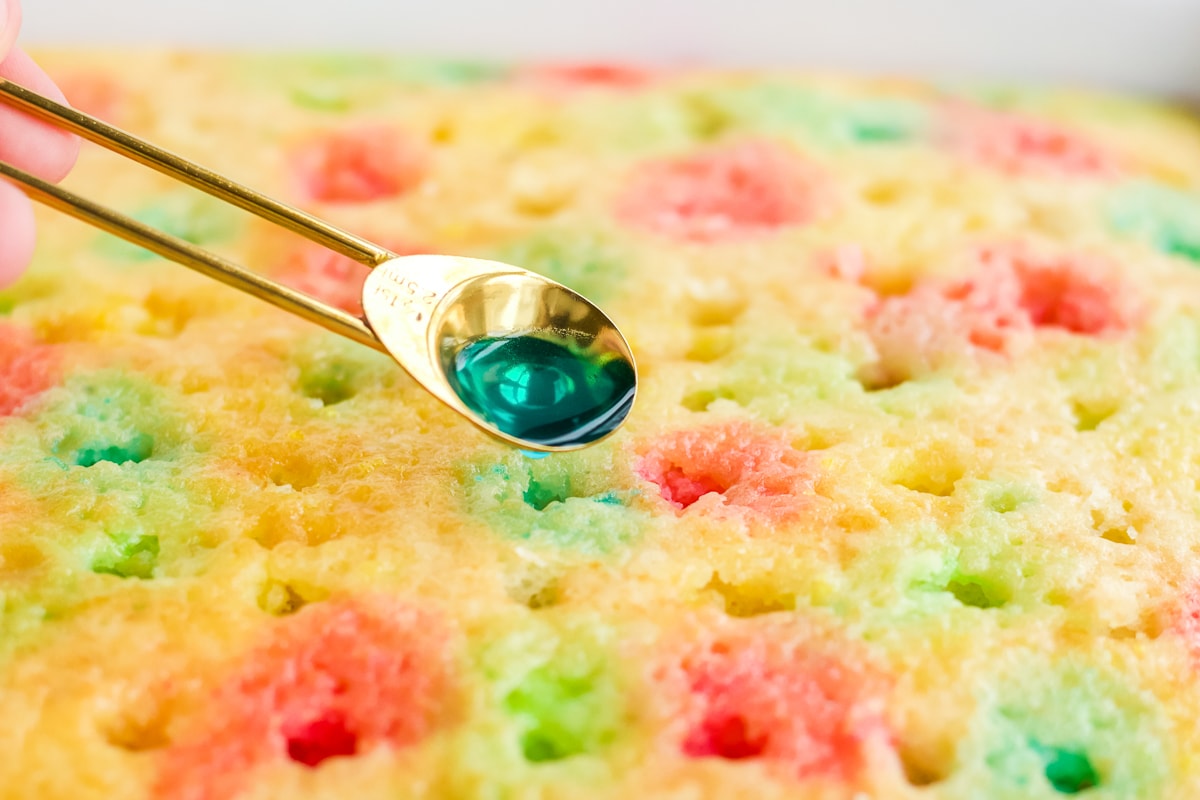 measuring spoon with blue jello as a liquid pouring it onto a cake.