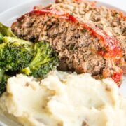 2 slices of meatloaf with mashed potatoes and broccoli on a white plate.