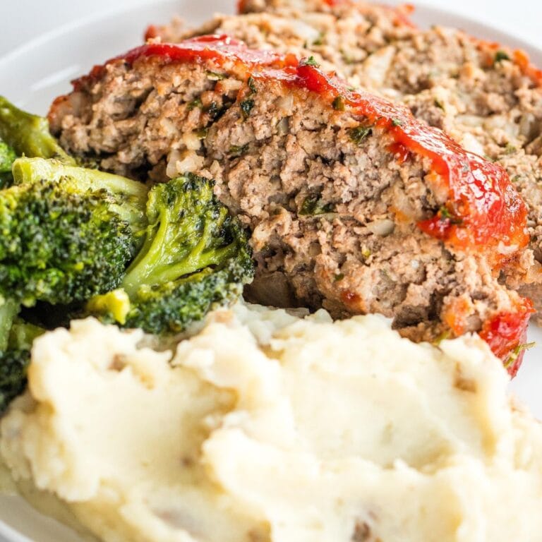 2 slices of meatloaf on a white plate with mashed potatoes and broccoli.