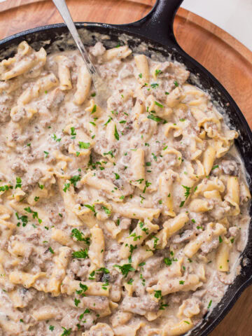Close up photo of ground beef stroganoff with pasta in a cast iron skillet, garnished with fresh parsley.