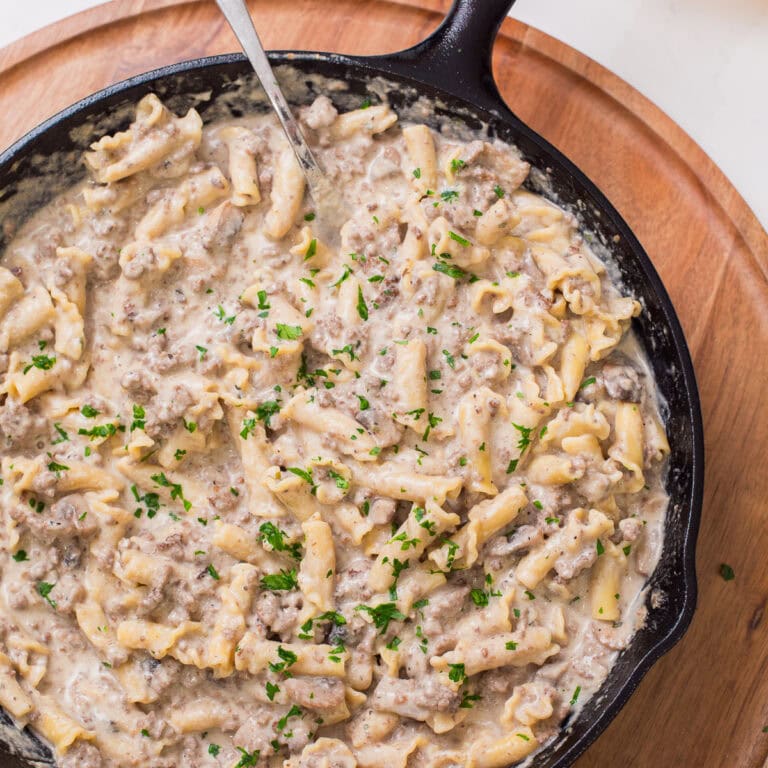Close up photo of ground beef stroganoff with pasta in a cast iron skillet, garnished with fresh parsley.