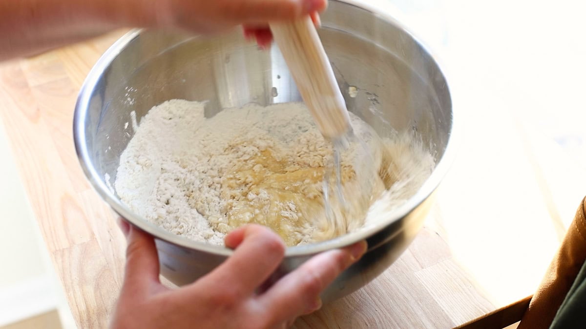 Batter being stirred into a bowl of flour using a whisk, partway through mixing the dry and wet ingredients.