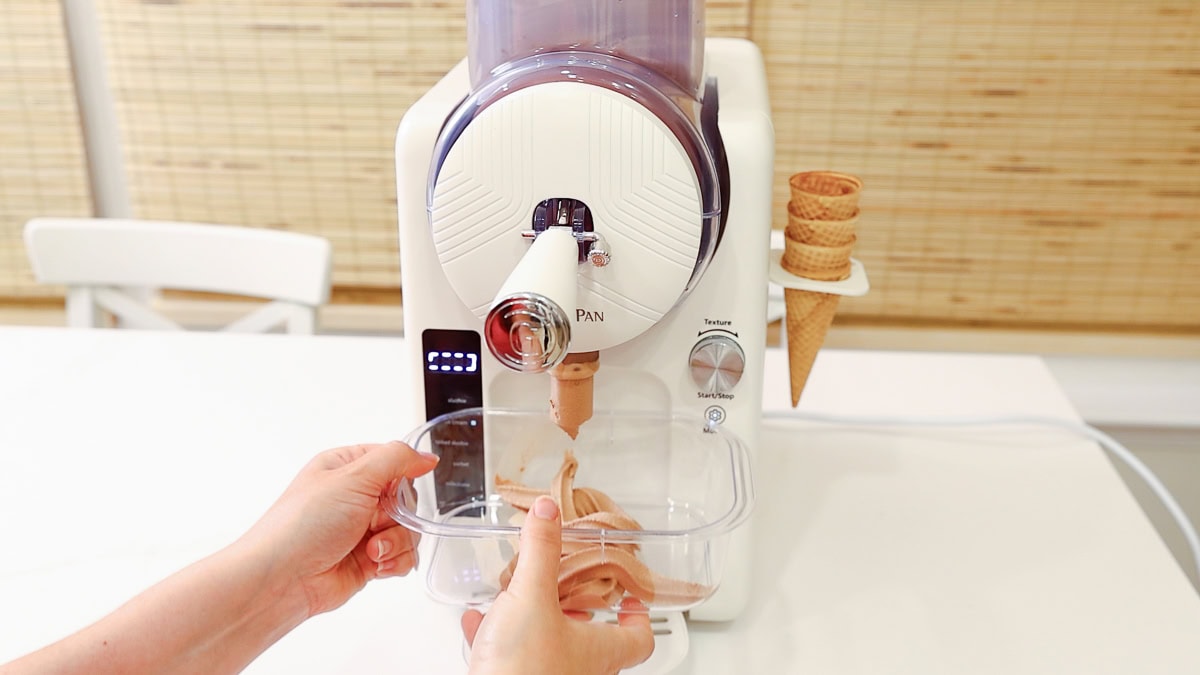 GreenPan Frost machine dispensing chocolate ice cream into a freezer-safe storage container.