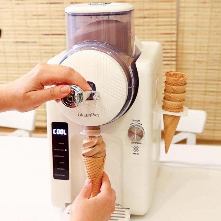 Two hands dispensing chocolate soft serve ice cream from the GreenPan Frost ice cream and frozen treat maker into a sugar cone.