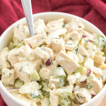 Mixed salad of chicken, eggs, celery, and herbs, with red onion pieces, with a red cloth background.