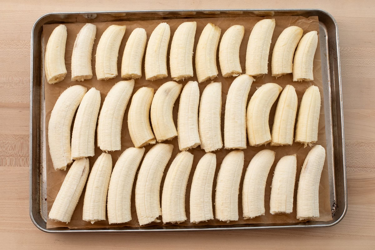 Overhead view of peeled bananas laid out evenly on a baking sheet lined with parchment paper.