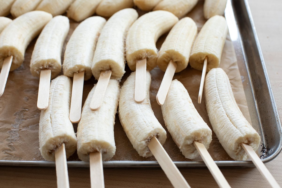 Close-up of banana halves with wooden popsicle sticks inserted, showing texture of frozen fruit.