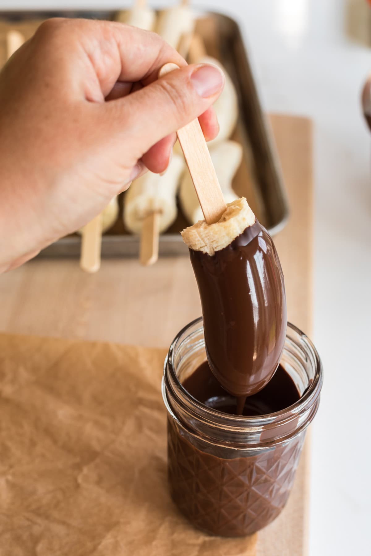 Hand lifting a frozen chocolate covered banana from a glass filled with chocolate.