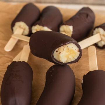 Close-up of chocolate-covered banana pops, focusing on the creamy banana interior of the bitten one.