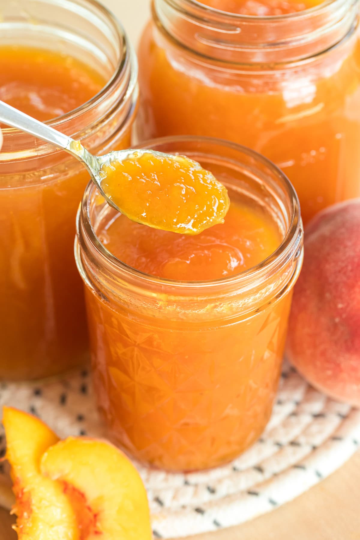 Close-up of a spoonful of peach jam above a jar, surrounded by jars of jam and peaches.