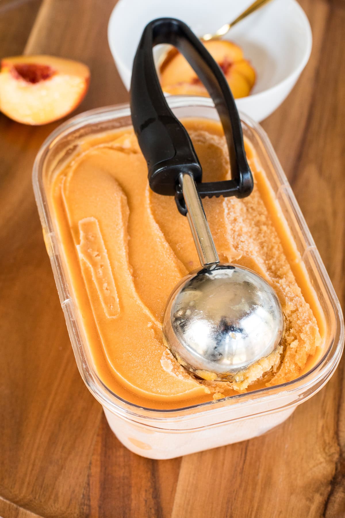 A container of homemade peach sorbet with an ice cream scoop inside, ready to serve.