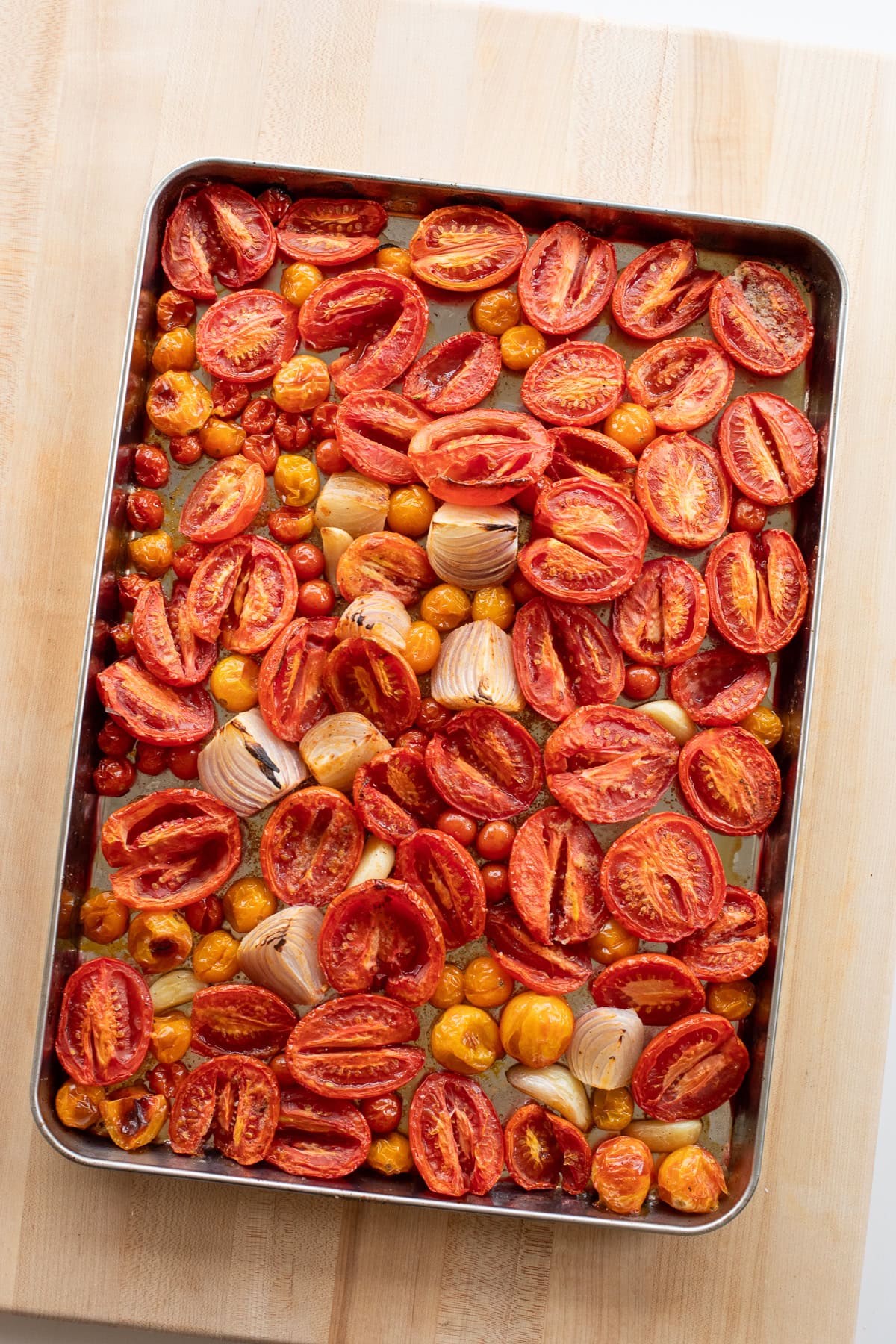 Sheet pan of roasted Roma and cherry tomatoes with onions and garlic, caramelized and ready for soup.