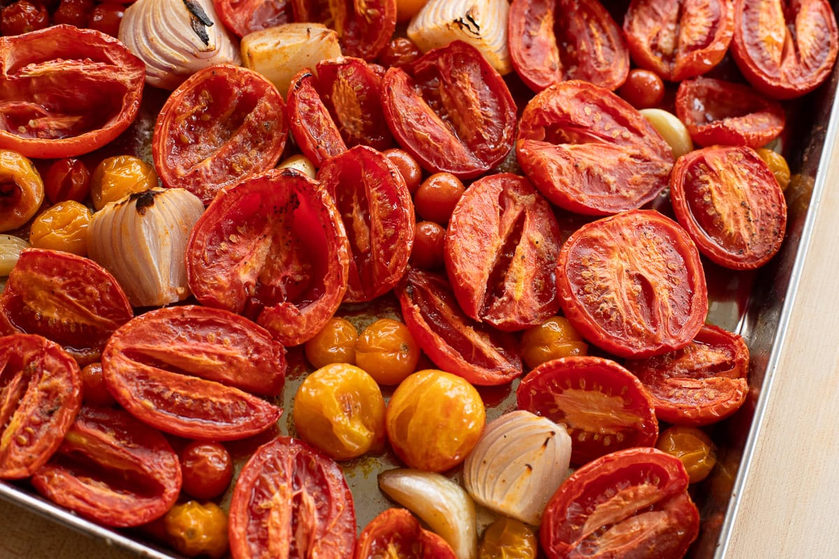 Overhead shot of roasted tomatoes and onions on a sheet pan, showing their rich color and caramelization.