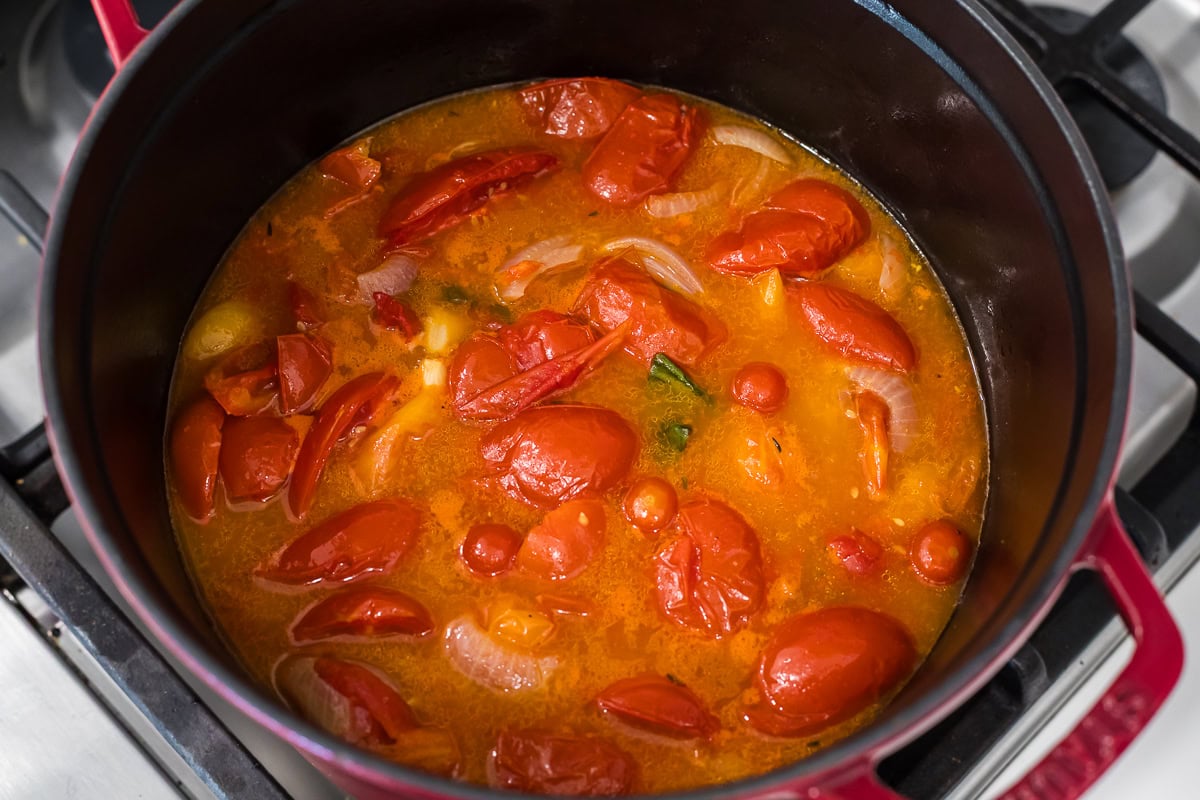 Close-up of roasted tomatoes, onions, and garlic simmering together in a red Dutch oven before blending.