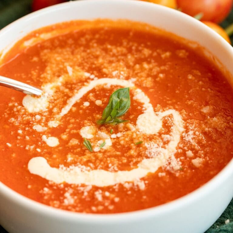Bowl of creamy roasted tomato soup topped with a swirl of cream, fresh basil, and Parmesan cheese.