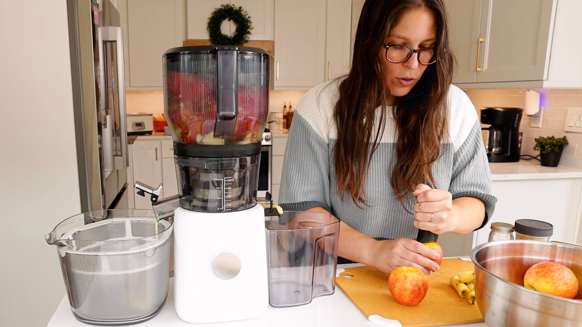 Woman preparing apples beside nama j2 juicer filled with apples in a kitchen.