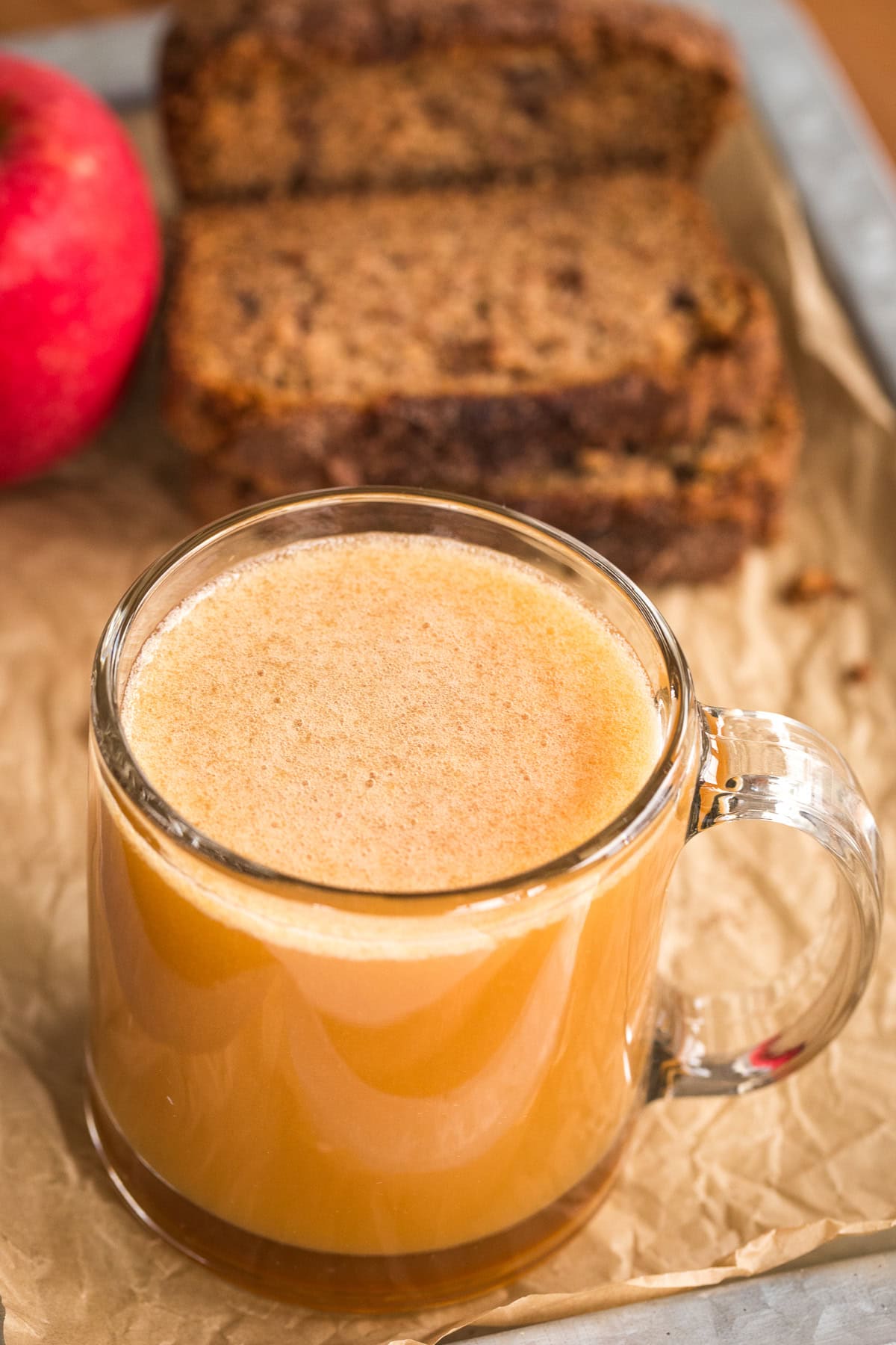 Close-up of a mug filled with apple cider with bread and apple in the background.