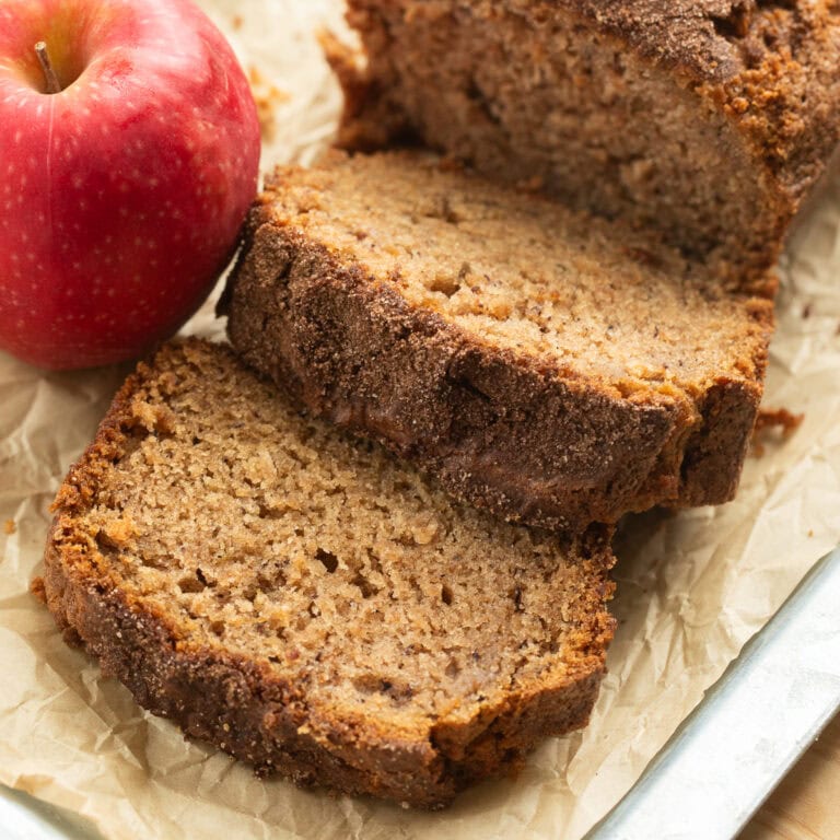 Slices of apple cinnamon bread on parchment with a red apple beside them.