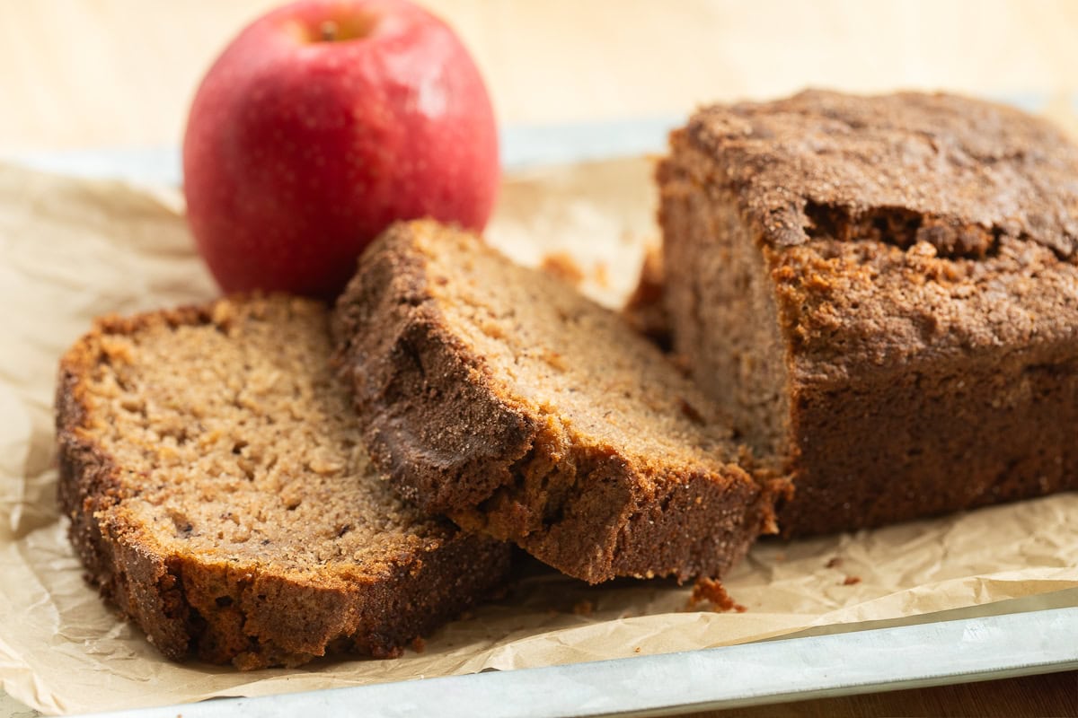 Two slices of apple cinnamon bread in front of a loaf with a red apple.