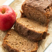 Apple cinnamon bread loaf with several slices cut, red apple on the side.