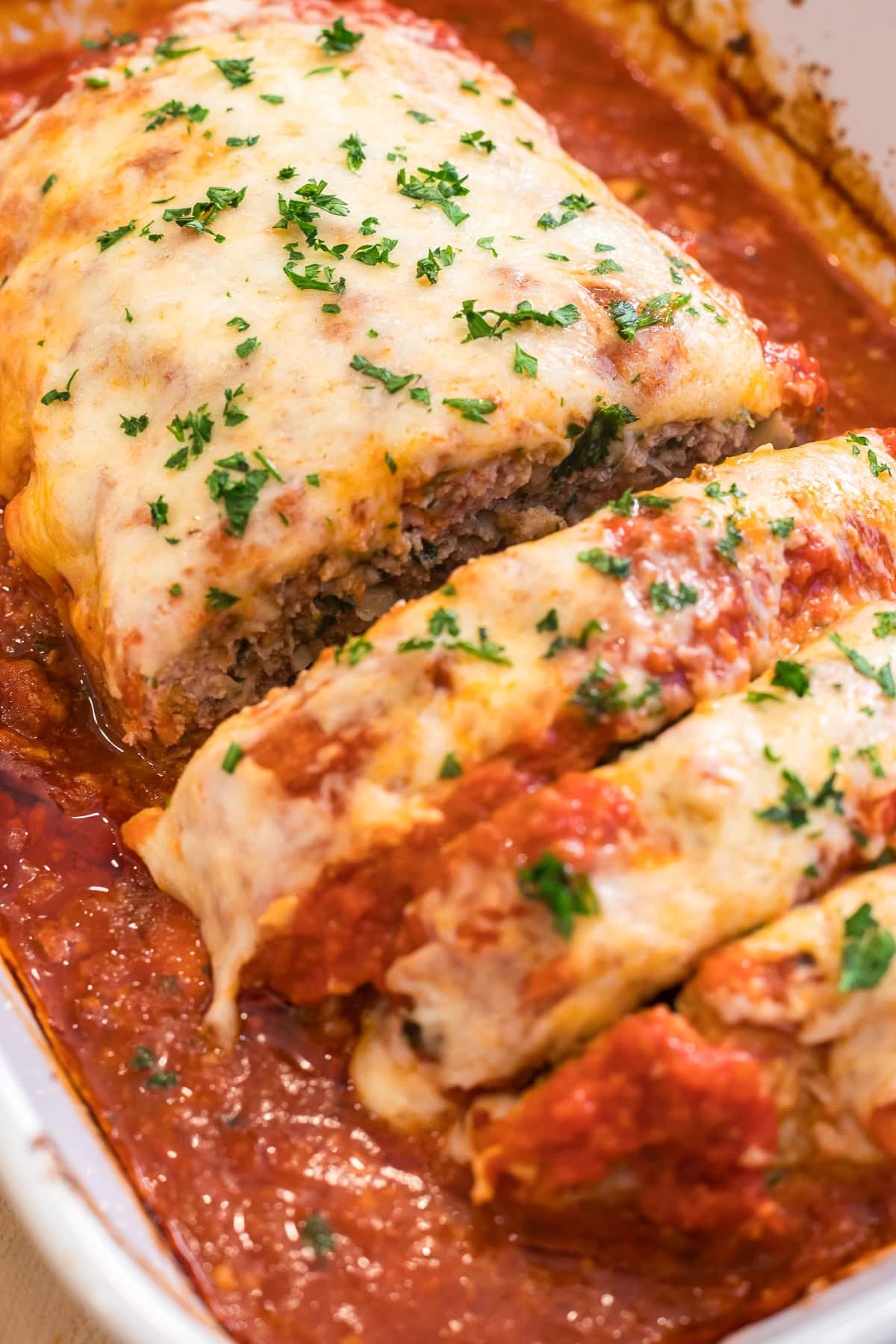 Close-up of Italian meatloaf in casserole dish with melted mozzarella and parsley freshly baked and sliced.