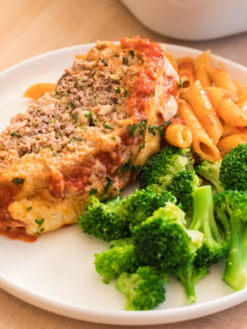 Italian baked meatloaf sliced on a white plate with broccoli and penne.
