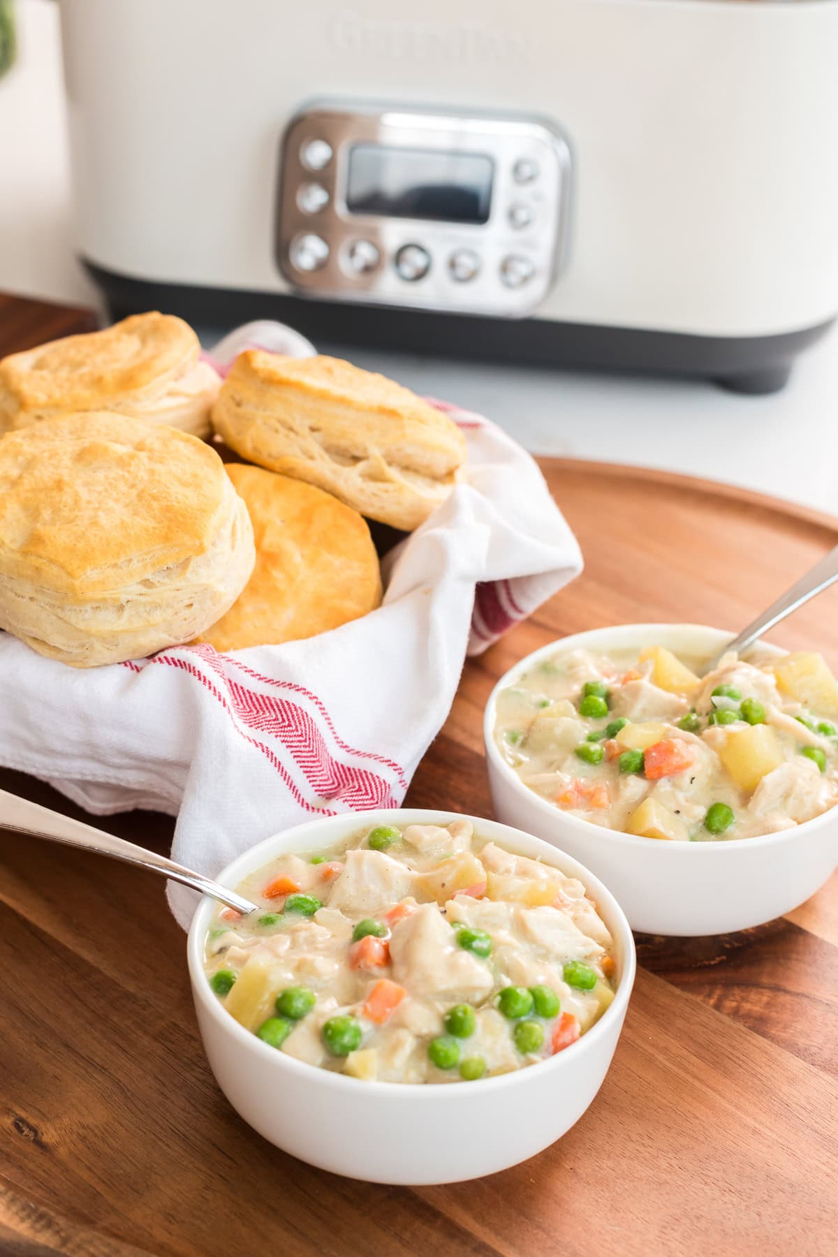 Hearty slow cooker chicken pot pie served in bowls with homemade-style biscuits on a wooden board, easy family dinner idea.