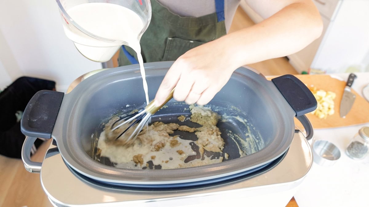 Milk being poured into a roux base in the GreenPan Elite slow cooker to make creamy chicken pot pie filling from scratch.