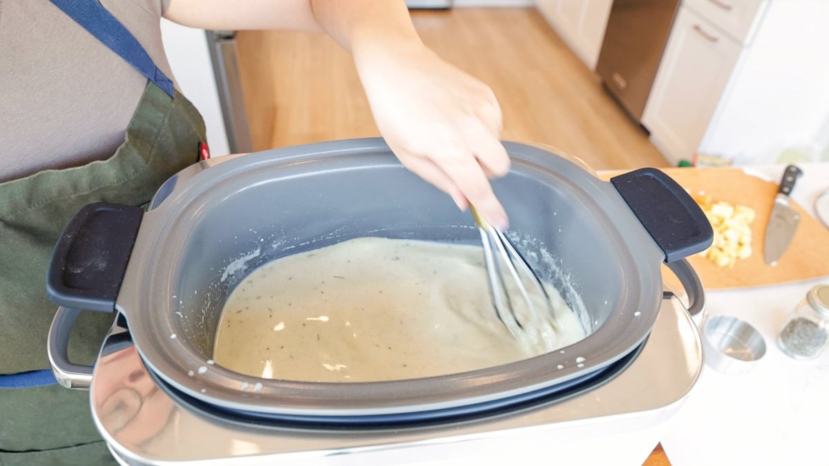Homemade condensed cream of chicken soup being whisked inside the GreenPan Elite slow cooker, forming the base for chicken pot pie filling.